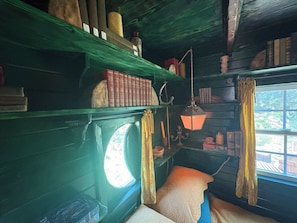 Et værelse med et vindue, en seng, en reol med bøger og en hængende lampe.