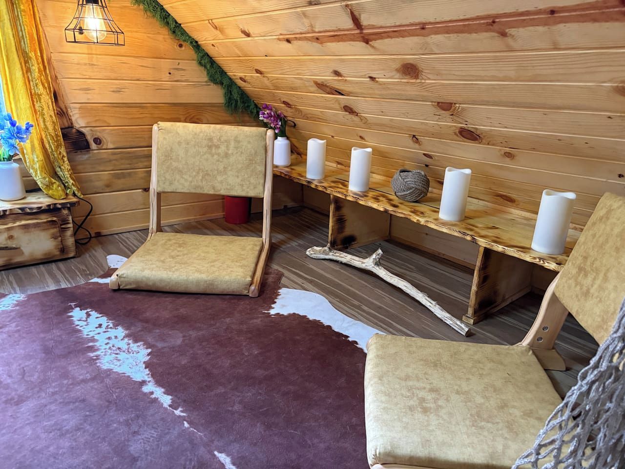 Tunnelmallinen mökin sisustus, jossa on puuseinät, kynttilöillä koristeltu penkki ja kaksi tuolia.