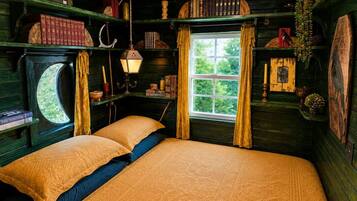 Una habitación con cama, una ventana con cortinas y estantes con libros y objetos decorativos.
