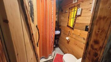 A wooden cabin bathroom with a toilet, sink, and a shower curtain.