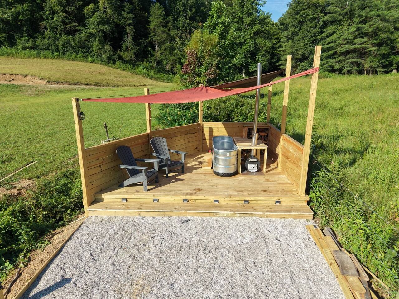 A wooden deck with outdoor seating, a metal barrel, and a red canopy.