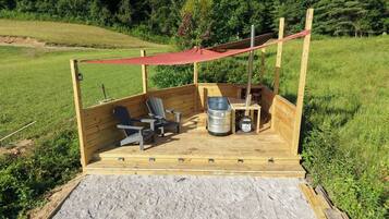 A wooden deck with outdoor seating, a metal barrel, and a red canopy.