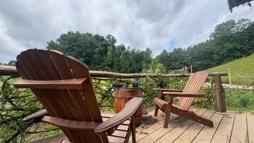 A wooden deck with Adirondack chairs and a barrel, overlooking a lush green landscape.