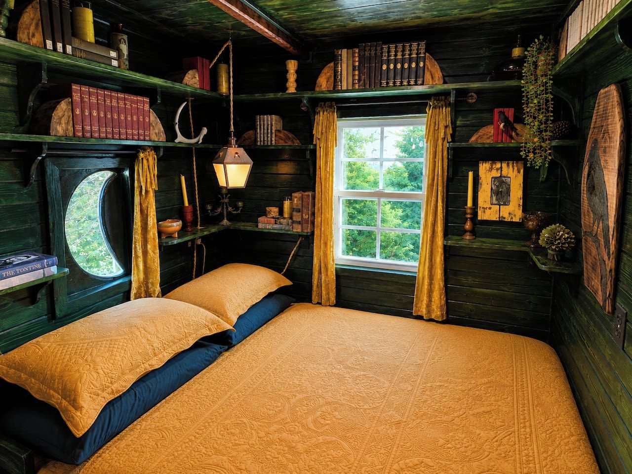 A cozy room with a large bed, a window with curtains, and shelves with books and decorative items.
