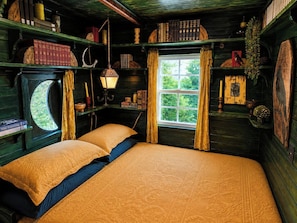 A cozy room with a large bed, a window with curtains, and shelves with books and decorative items. - The Crooked Cabin - Wood-Fired Hot Tub near RRG (Lee County)