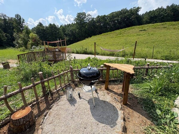 A barbecue grill in a grassy outdoor area with a wooden fence and a wooden bench.
