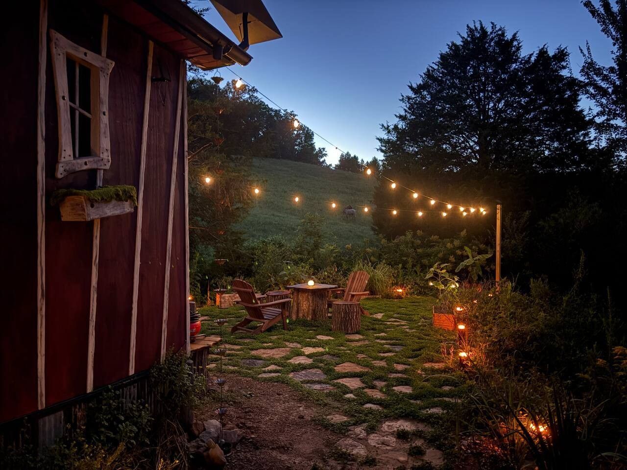 Un espace extérieur aménagé dans un style rustique, avec un chemin de pierres, des chaises en bois et des guirlandes lumineuses.