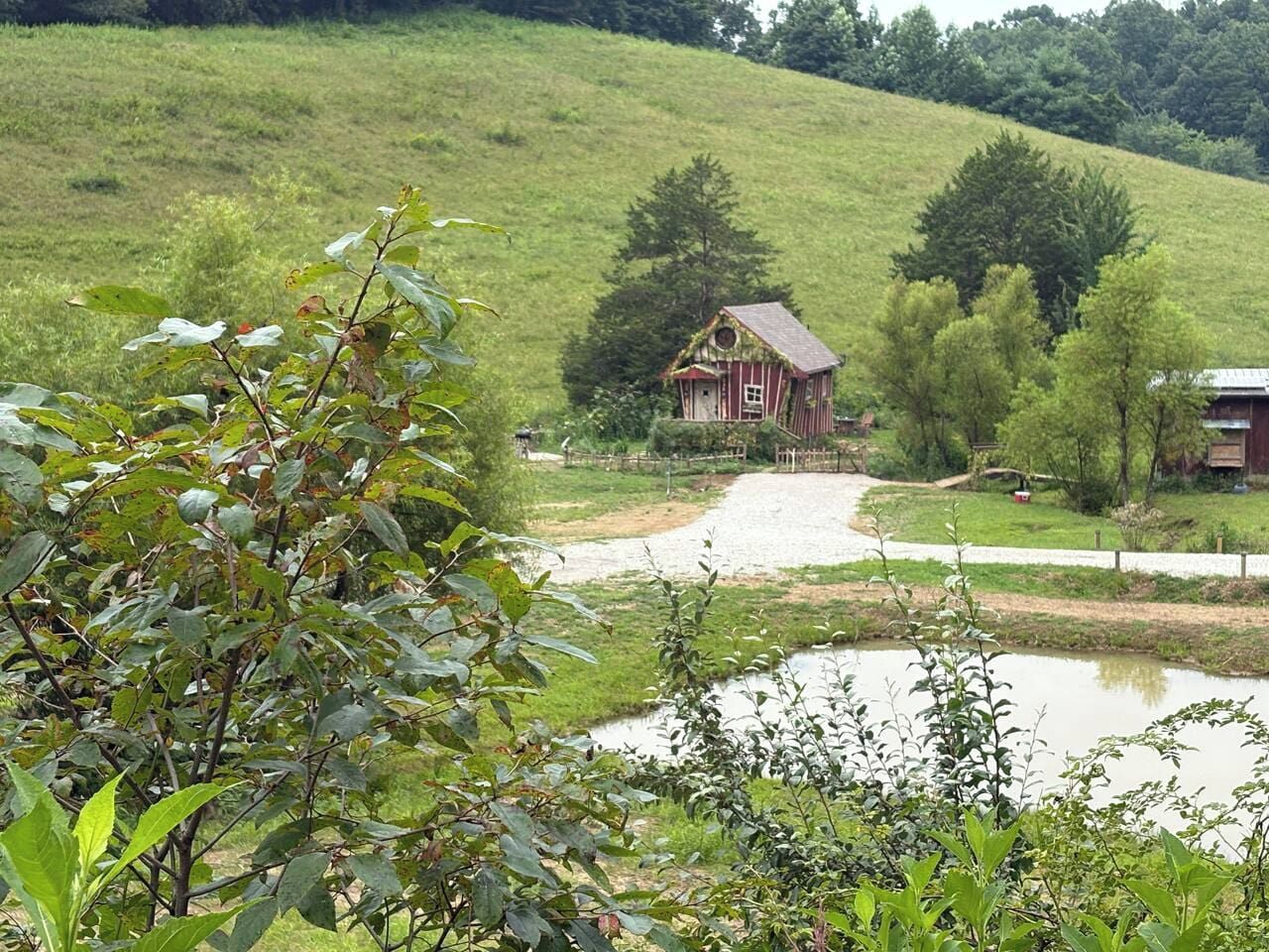 A rural landscape with a red barn, a pond, and a grassy hill.