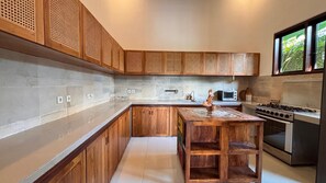 A modern kitchen with wooden cabinetry, a central island, and built-in appliances. - Peaceful Family 4 Bedrooms Private Pool Villa with Jungle View (ubud)