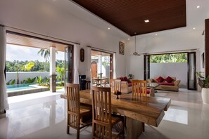 Amplia sala de estar con una mesa de comedor de madera, asientos cómodos y vistas a una piscina y zonas verdes.