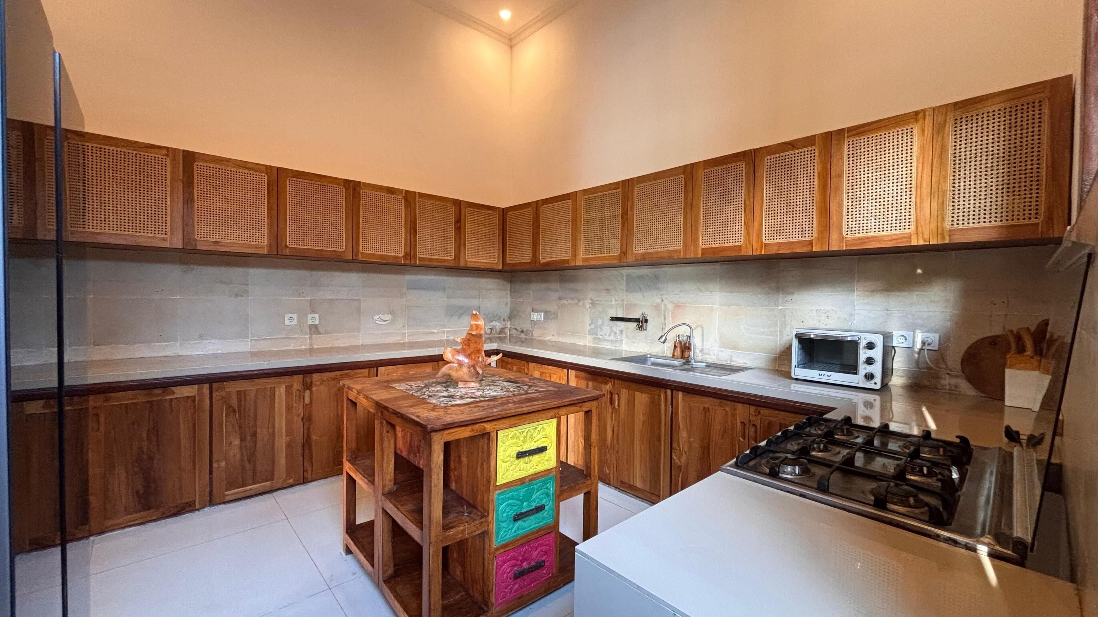 Een keuken met houten kastjes, een gasfornuis, een magnetron en een kleurrijke opbergunit.
