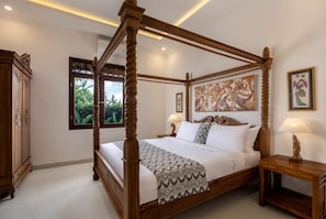 A four-poster bed with a patterned bedspread, two bedside tables with lamps, and artwork on the walls.