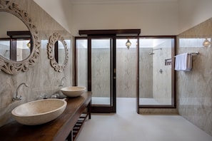 Ein modernes Badezimmer mit zwei großen, ovalen Waschbecken, einer Dusche und einer Duschkabine aus Glas.
