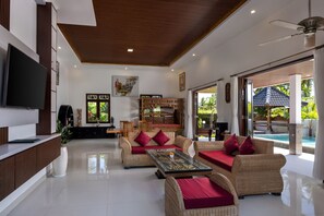 A spacious living area with a flat-screen TV, wicker furniture, and a large window offering a view of the outdoors.