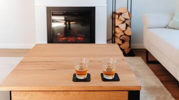 Ein Holztisch mit zwei Gläsern bernsteinfarbener Flüssigkeit, vermutlich Whiskey, auf schwarzen Untersetzern.