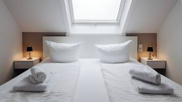 A twin room with a skylight, two bedside tables with lamps, and neatly folded towels.