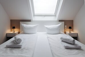 Ein Doppelzimmer mit Oberlichter, zwei Nachttische inklusive Lampen und ordentlich gefaltete Handtücher.