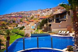 A swimming pool with lounge chairs, surrounded by a landscaped garden and a hillside of colorful buildings. - Pueblo Bonito Montecristo Luxury Villas - All Inclusive (Cabo San Lucas)
