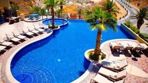 Una piscina amb gandules i palmeres, envoltada per un paisatge montanyós.