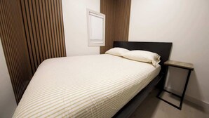 Un lit avec une tête de lit, une table de chevet et un luminaire fixé au mur.