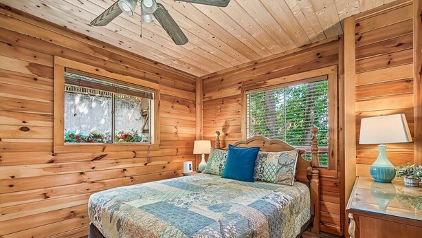 A wooden cabin bedroom with a bed, windows, and a ceiling fan. - Halfway to Heaven | Hot Tub, Game Room & Views (Gatlinburg)