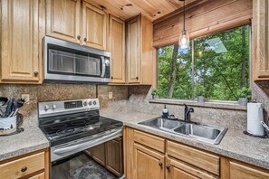 A kitchen with wooden cabinets, a stainless steel sink, a stove, and a microwave. - Halfway to Heaven | Hot Tub, Game Room & Views (Gatlinburg)