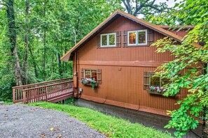 A wooden cabin with a porch, surrounded by dense forest. - Halfway to Heaven | Hot Tub, Game Room & Views (Gatlinburg)