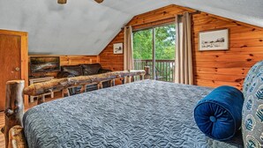 A bedroom with a sloped ceiling, a bed with a patterned bedspread, a wooden headboard, a ceiling fan, and a window with curtains. - Halfway to Heaven | Hot Tub, Game Room & Views (Gatlinburg)