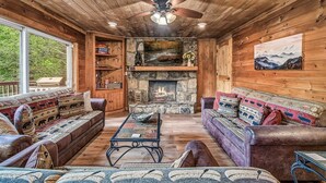 A cozy cabin interior with a stone fireplace, wooden walls, and a ceiling fan. - Halfway to Heaven | Hot Tub, Game Room & Views (Gatlinburg)