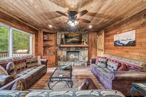 A cozy cabin interior with a stone fireplace, wooden walls, and a ceiling fan. - Halfway to Heaven | Hot Tub, Game Room & Views (Gatlinburg)