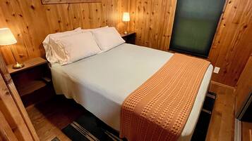 Une chambre dans une cabane en bois, comprenant un lit, des tables de chevet, une fenêtre et un appareil de climatisation.