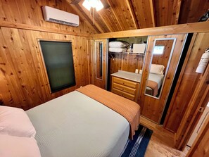 A wooden-paneled room with a bed, a dresser, a mirror, and an air conditioning unit.
