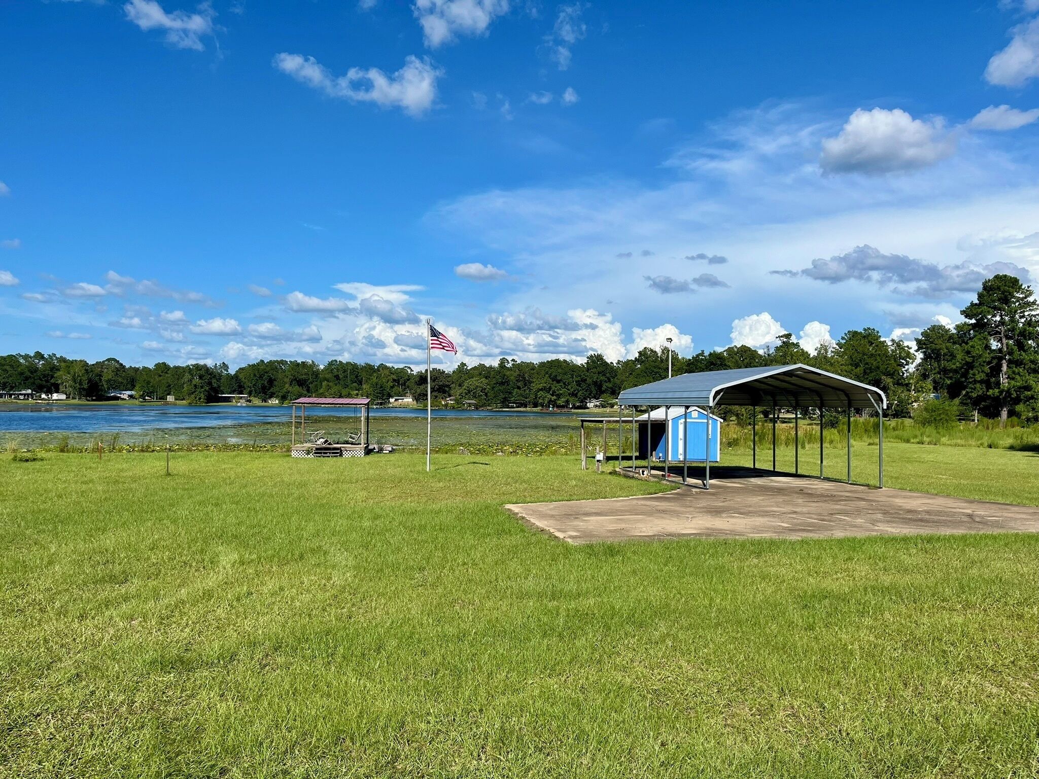 Une zone herbeuse avec un pavillon abrité, un mât portant le drapeau américain, et une étendue d'eau en arrière-plan.