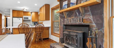 Una cocina con armarios de madera, una chimenea de piedra y un comedor con sillas de madera.