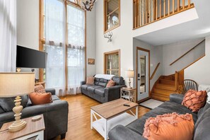 A spacious living room with a sofa set, a coffee table, a TV, and a staircase. - Paw Paw Mountain Lodge w/River Access & Fire Pit (Paw Paw)