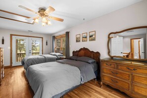 Ein Schlafzimmer mit zwei Betten, einer Holzkommode, einem Deckenventilator und einem großen Fenster.