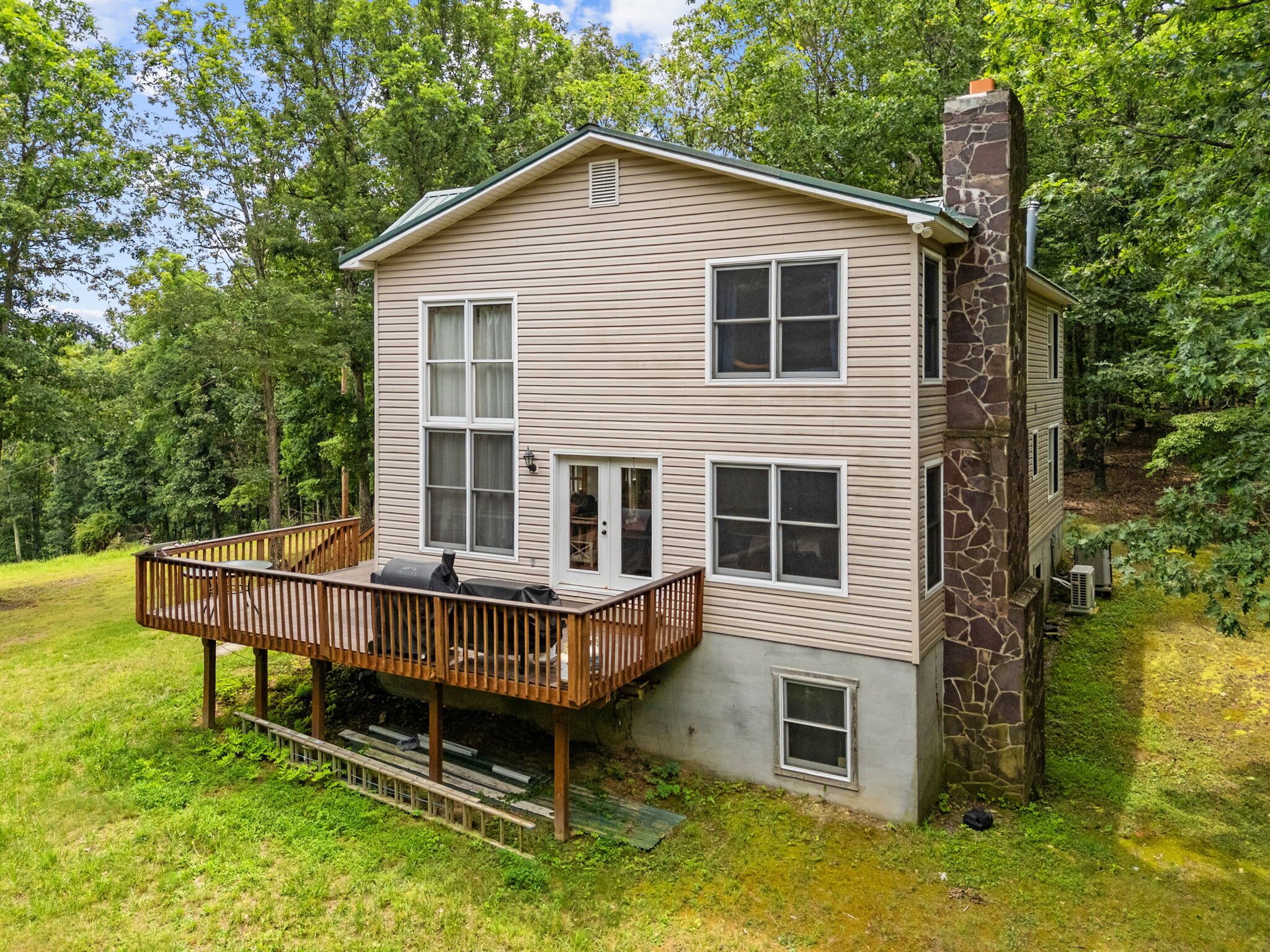 A two-story house with a stone chimney, a deck, and a small porch.