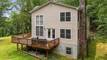 A two-story house with a stone chimney, a deck, and a small porch.