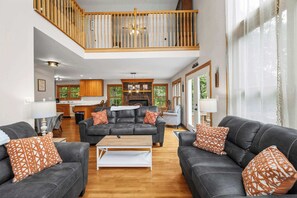 A spacious living room with a high ceiling, a fireplace, and a view of the outdoors. - Paw Paw Mountain Lodge w/River Access & Fire Pit (Paw Paw)
