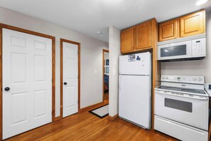 Une cuisine de taille réduite, avec des appareils électroménagers blancs, des meubles en bois et une porte visible donnant sur une autre pièce.