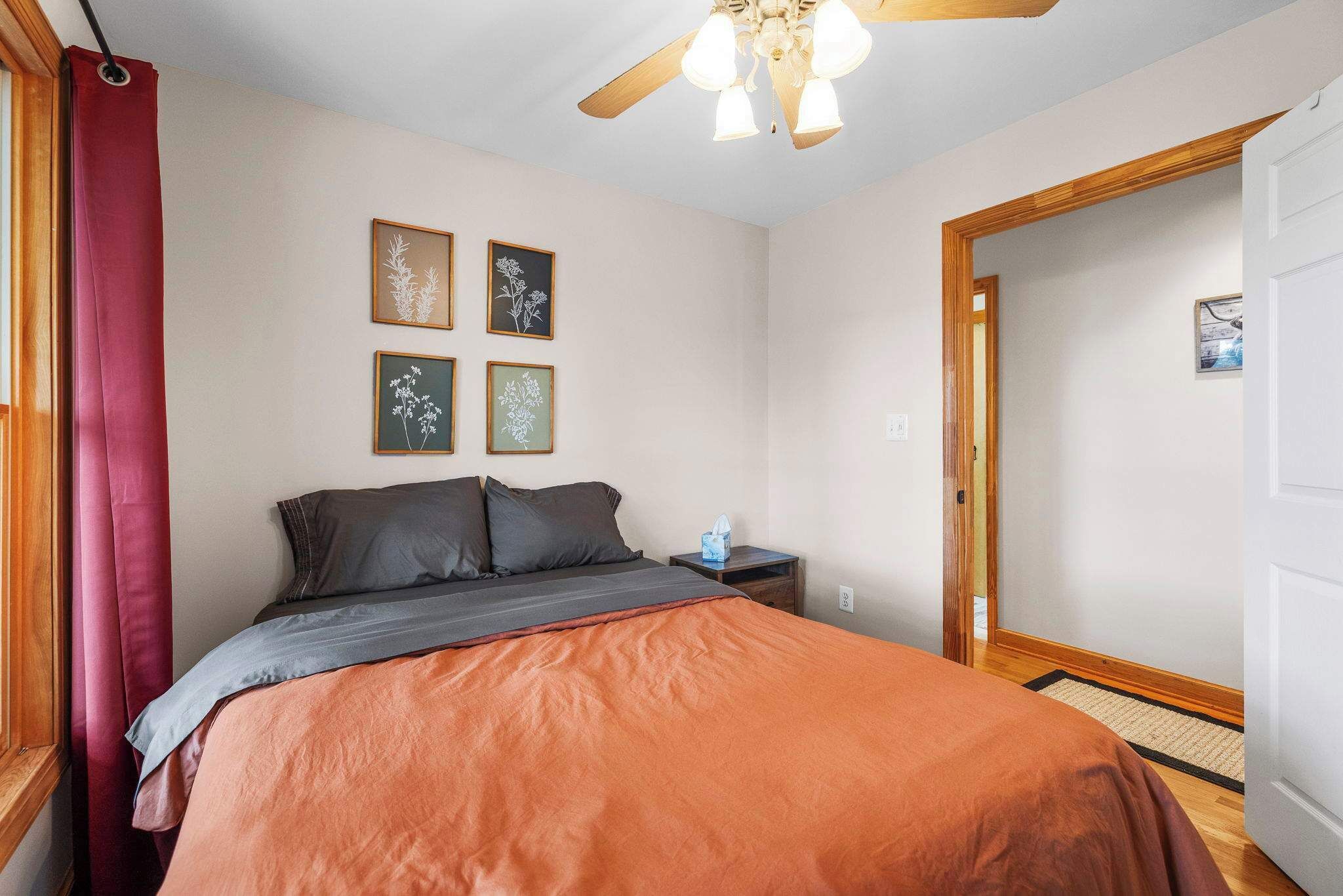 Quarto com cama, mesa de cabeceira, ventilador de teto e quadros nas paredes.