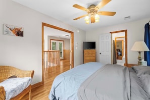 Une chambre à coucher comprenant un lit, un téléviseur, une commode et un ventilateur de plafond.