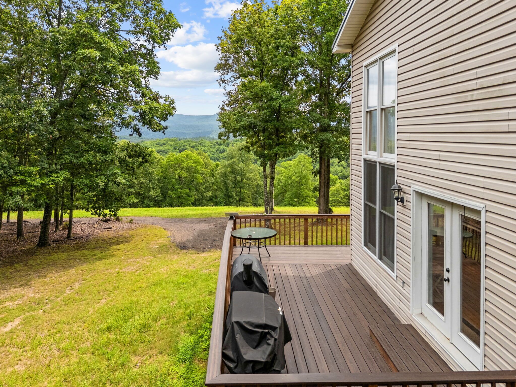 Eine Terrasse mit Grill, Tisch und Blick auf einen Wald und Berge.