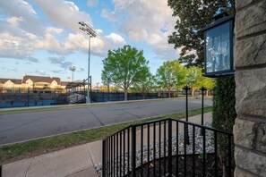A view of a swimming pool area with a fence, a basketball court, and a building with a stone facade. - Luxury Apartment B on TU Campus 2 Mins to downtown (Tulsa)