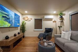 A living room with a flat-screen TV, a grey sofa, a wooden coffee table, and a black chair. - Luxury Apartment B on TU Campus 2 Mins to downtown (Tulsa)