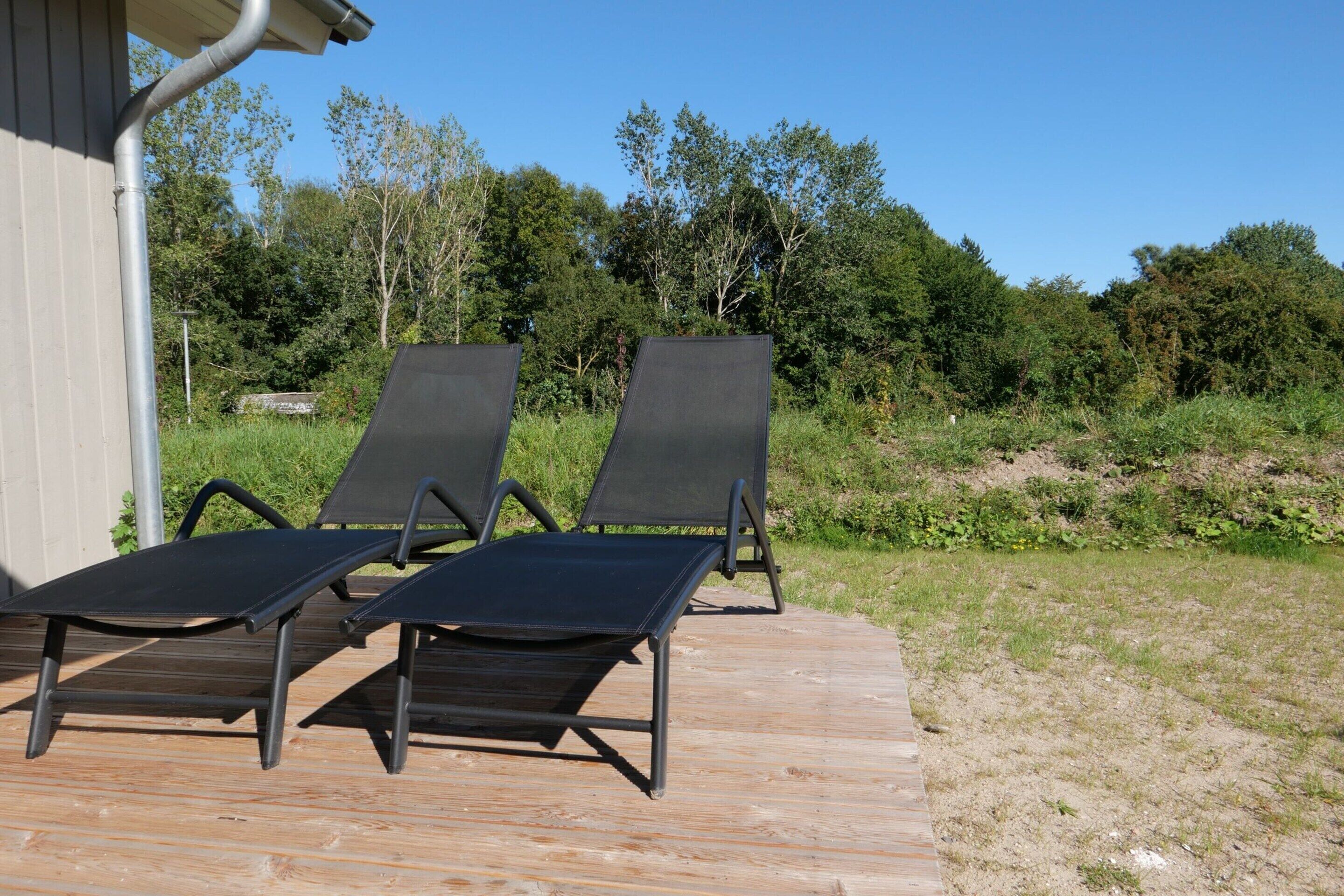 Zwei Liegestühle auf einer Holzterrasse mit Blick auf ein bewaldetes Gebiet.