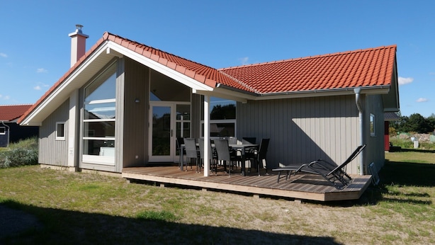 A modern house with a sloped roof, large windows, and a wooden deck with outdoor furniture. - Grossenbrode Meeresflucht (Grossenbrode)