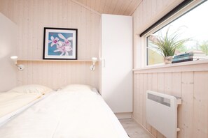 Ett sovrum med två sängar, ett fönster med utsikt över grönområden, ett element och en hylla med böcker och en växt.