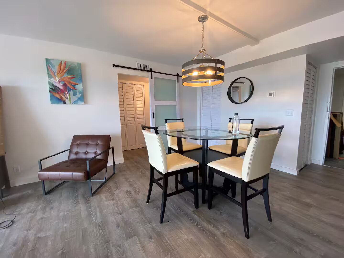 A dining area with a glass table and chairs, a hanging light fixture, and a door leading to another room.