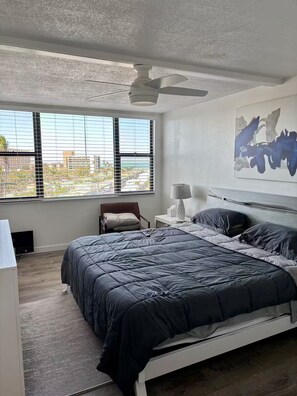 A bedroom with a bed, a chair, a bedside table, a lamp, and a window with blinds. - Resort amenities in siesta Key! (Siesta Key)